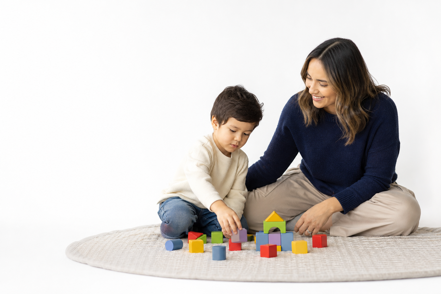 A young child and caregiver playing with colorful blocks on a floor mat in soft window light