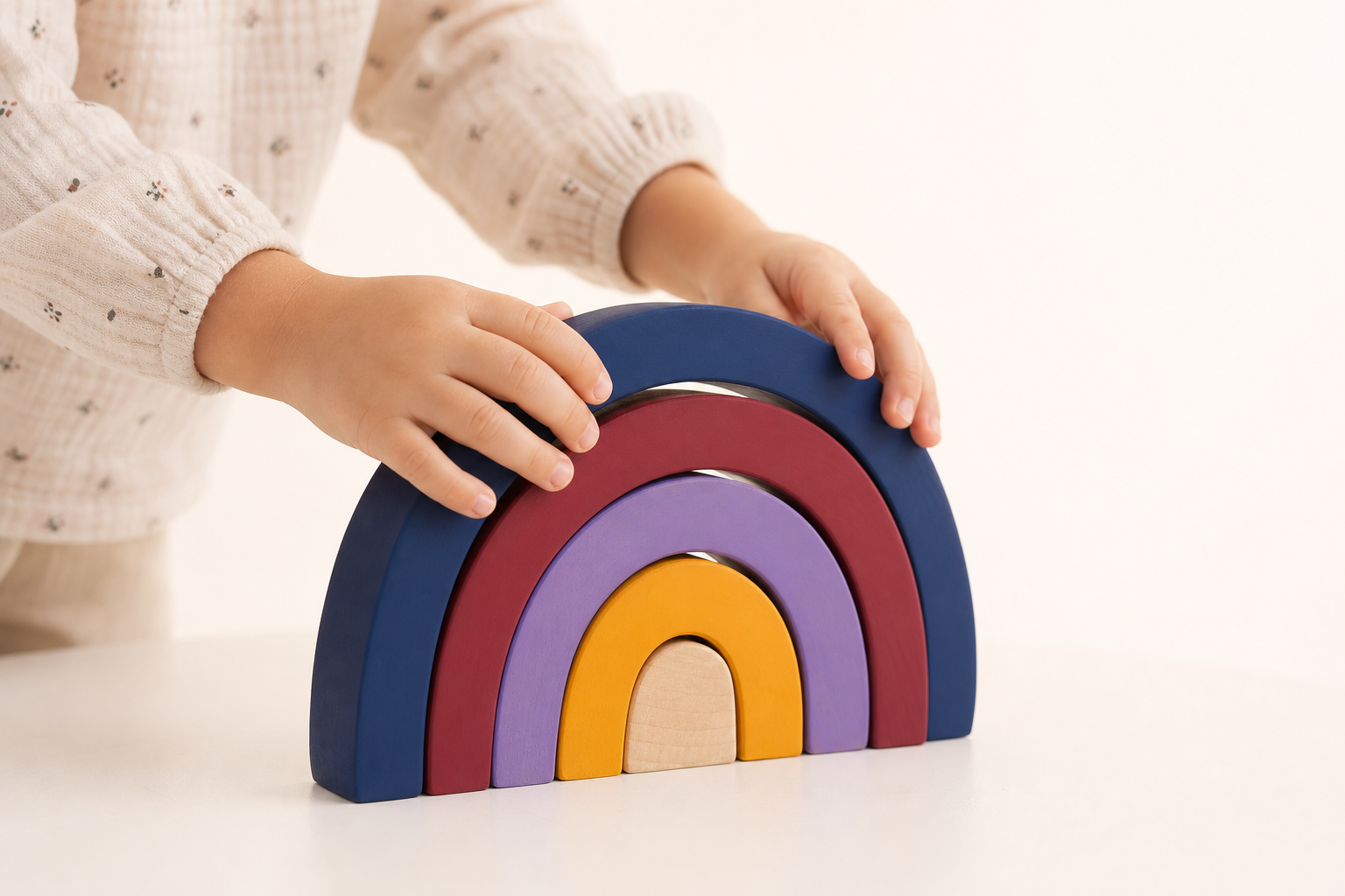 Close-up of a child’s hands stacking a wooden rainbow bridge toy